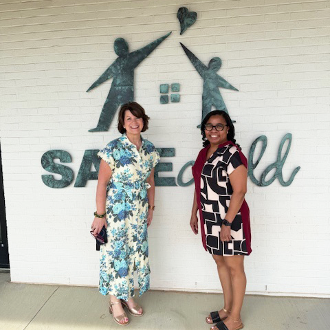 Two women in dresses pose in front of Safechild logo on wall